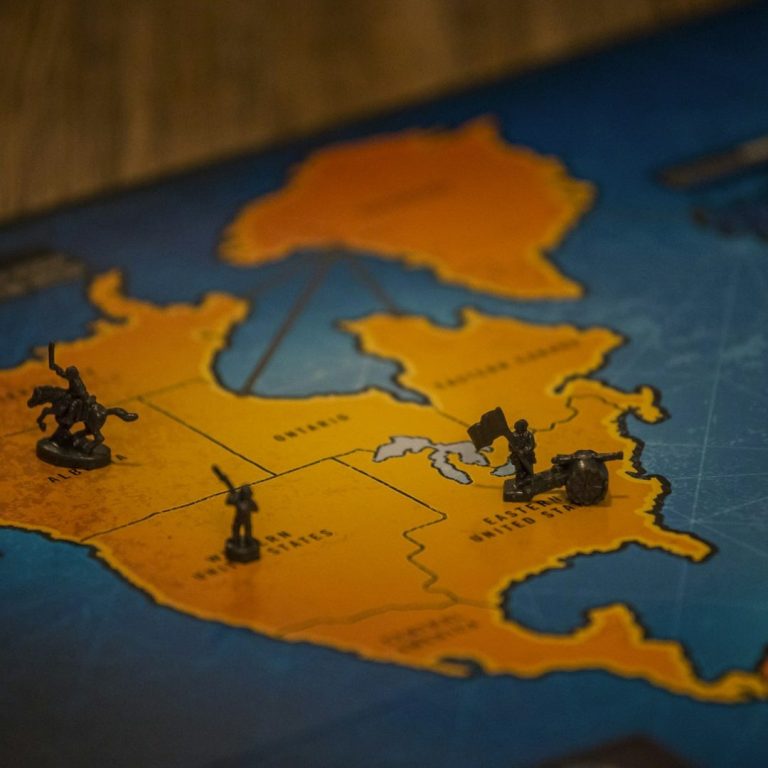 risque pays Carte de jeu avec figurines sur une île et des marins, territoire en orange et bleu.