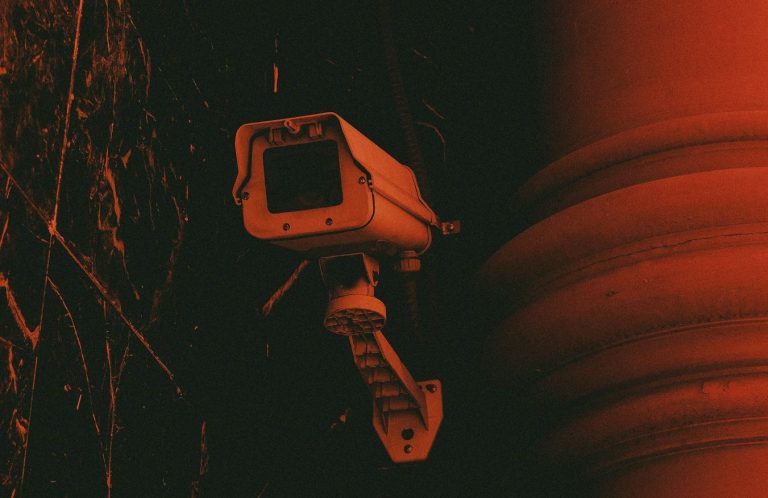 espionnage RivierX Caméra de surveillance fixée sur un mur sombre, éclairée par une lumière rouge.