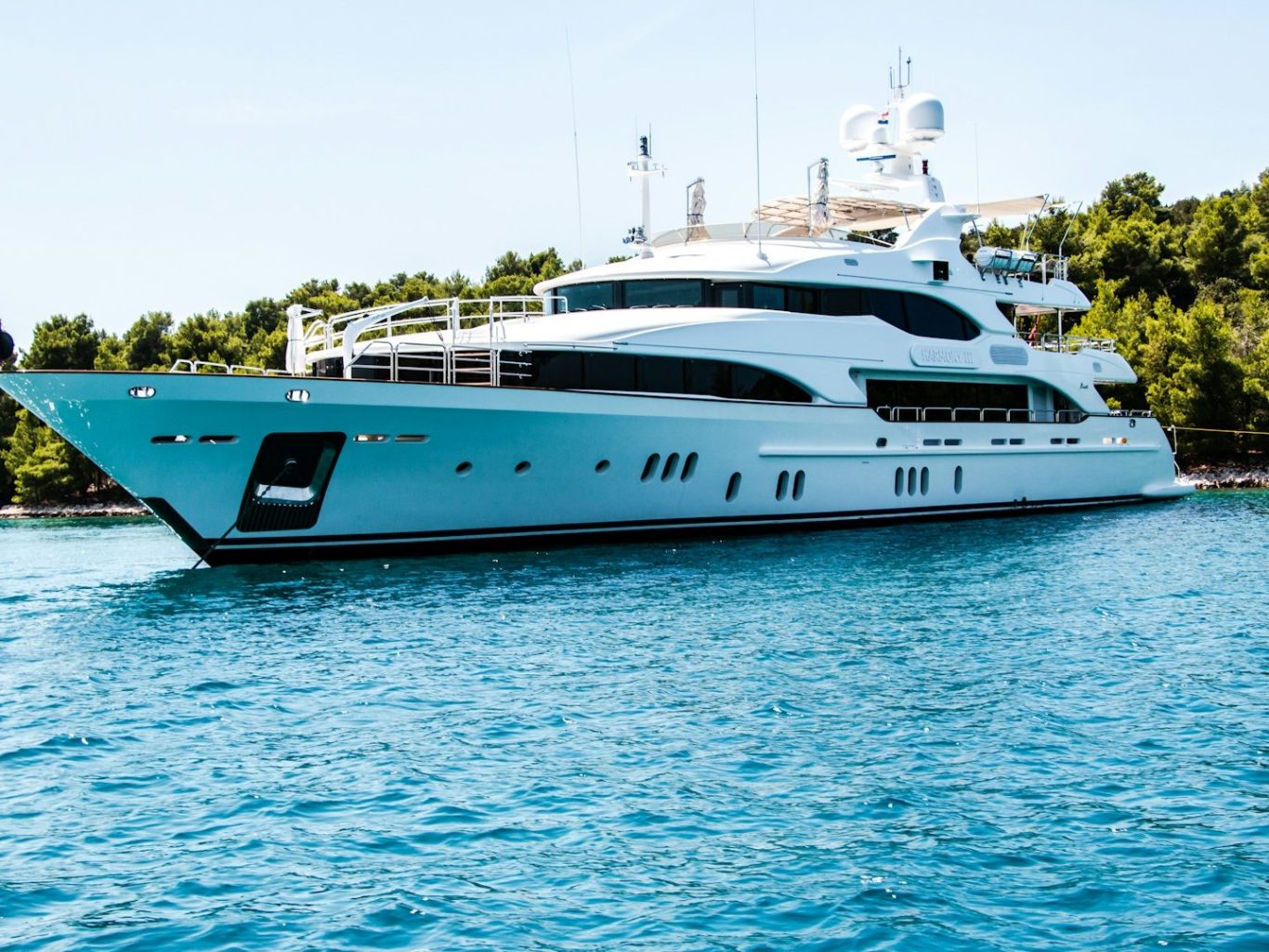 Marine HVAC Yacht blanc de luxe amarré dans une eau turquoise, entouré de verdure.