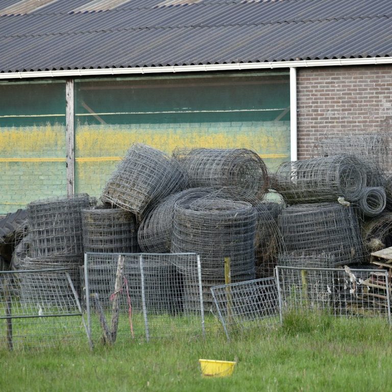Dépot RivierX Piles de pneus usés empilés derrière une barrière dans un champ.